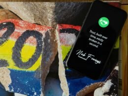 Schwarzes iPhone 5 auf blau-gelb-rot gemustertem Felsen, fotografiert von oben, geeignet für Tech- und Marketingartikel