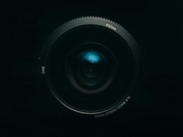 Schwarzes Kameraobjektiv auf weißem Untergrund, formatfüllend und detailreich fotografiert, geeignet für Technikartikel