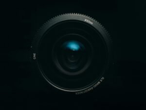 Schwarzes Kameraobjektiv auf weißem Untergrund, formatfüllend und detailreich fotografiert, geeignet für Technikartikel