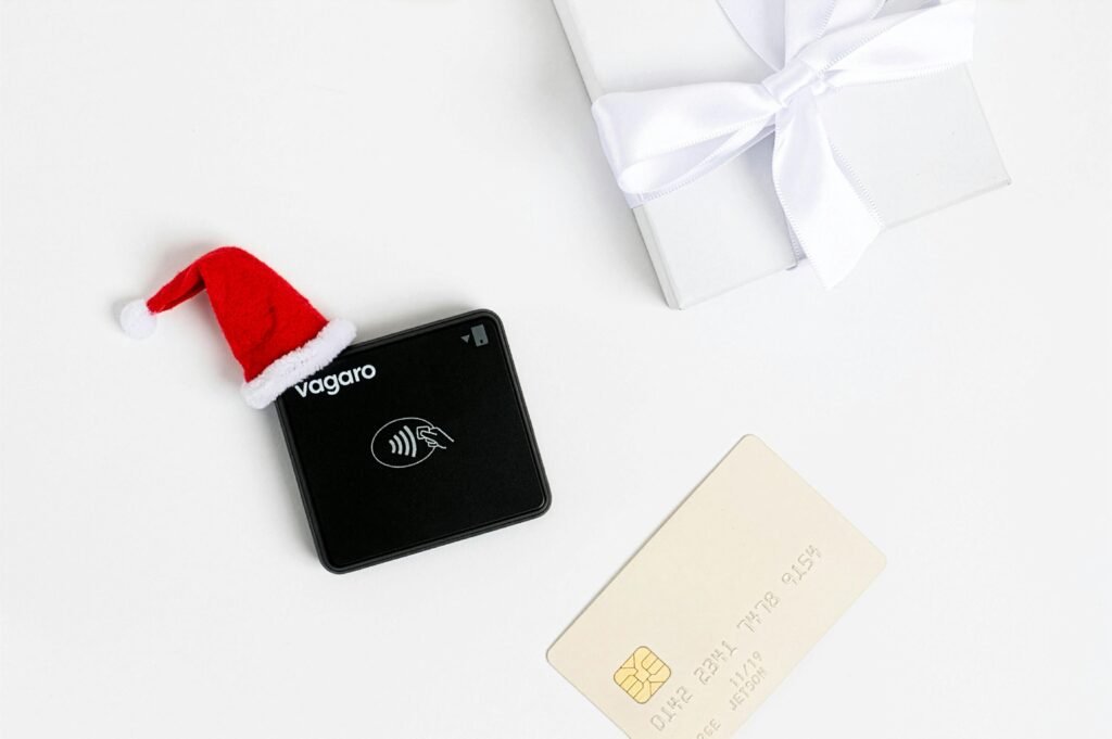 Schwarzes Zahlungsterminal mit Weihnachtsmütze und Geschenk, Symbol für festliche digitale Zahlungen im Handel