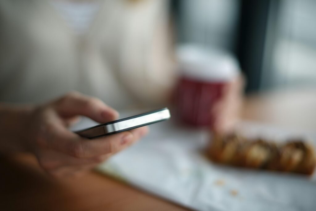 Person hält ein graues Smartphone in der Hand, Fokus liegt auf dem Gerät, im Hintergrund ist alles unscharf.