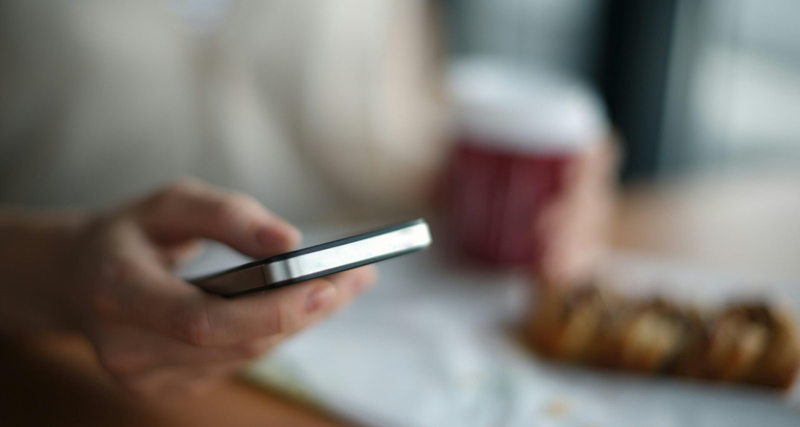 Person hält ein graues Smartphone in der Hand, Fokus liegt auf dem Gerät, im Hintergrund ist alles unscharf.