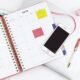 Silbernes iPhone 6, platziert auf einem weißen Spiralnotizbuch, aus der Vogelperspektive aufgenommen, klare Linien und Kontraste.