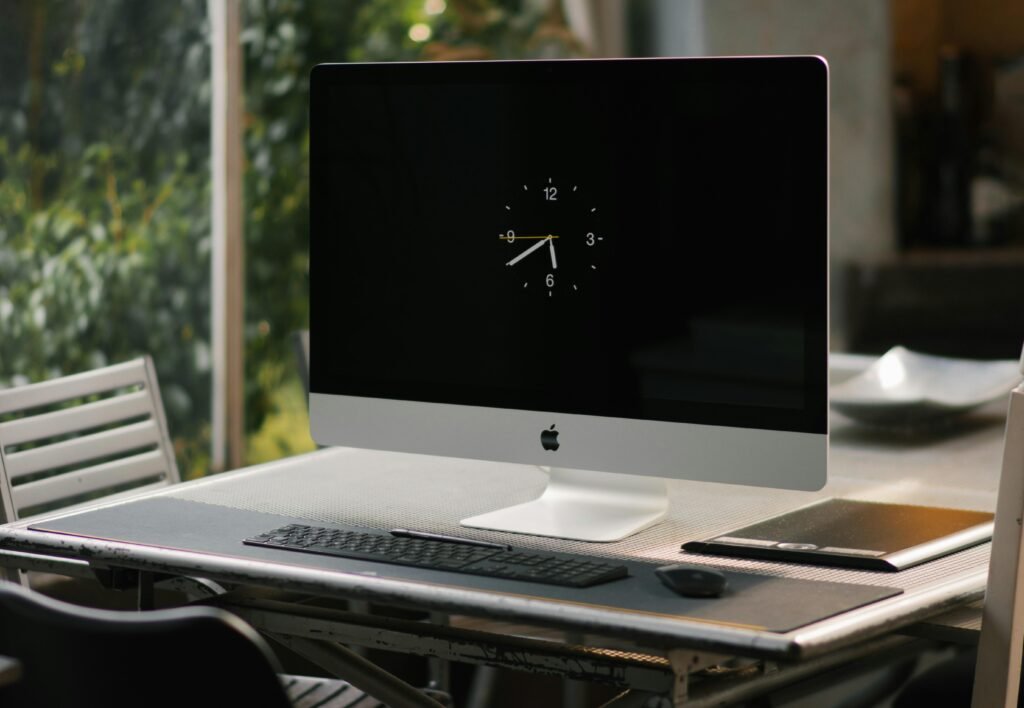 Silberner iMac steht auf einem braunen Holzschreibtisch in einem modernen Büro, Computer ist eingeschaltet.