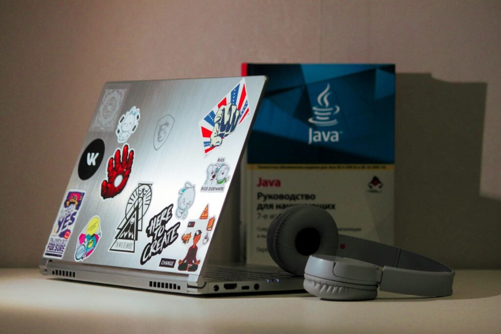 Silberner Laptop-Computer und graue kabellose Kopfhörer auf einem Schreibtisch für modernes digitales Arbeiten
