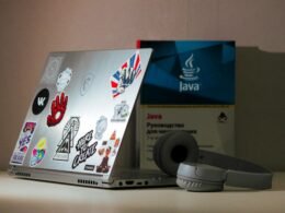 Silberner Laptop-Computer und graue kabellose Kopfhörer auf einem Schreibtisch für modernes digitales Arbeiten