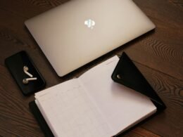 Silbernes MacBook und schwarzes iPhone 5 liegen nebeneinander auf einem Tisch – perfekte Kombination für produktives Arbeiten.