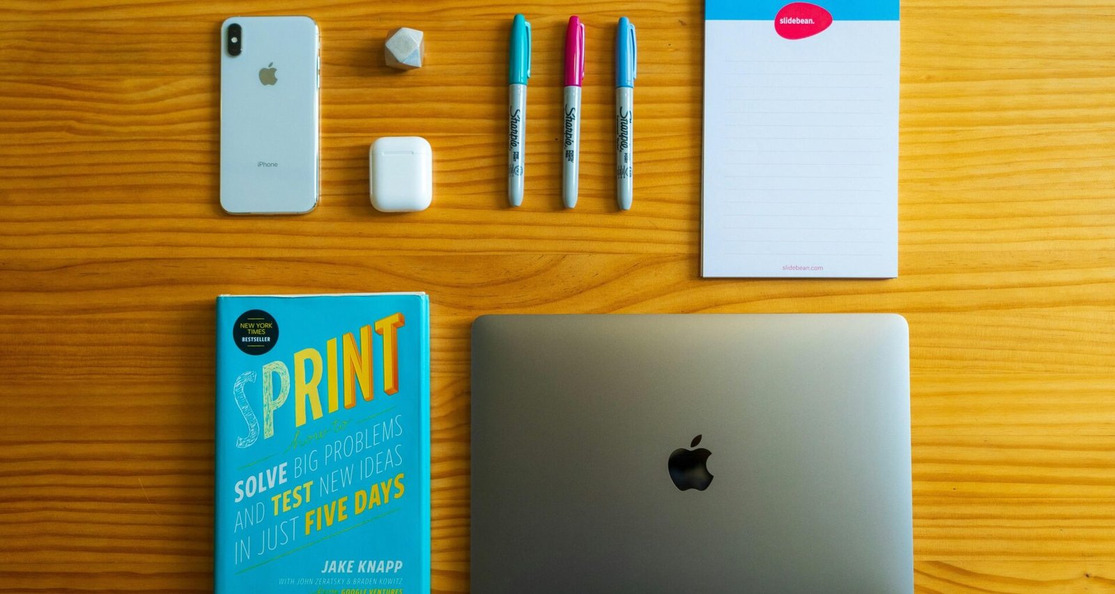 Silbernes MacBook neben einem weißen Notizbuch und mehreren Stiften auf einem Schreibtisch