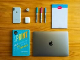 Silbernes MacBook neben einem weißen Notizbuch und mehreren Stiften auf einem Schreibtisch