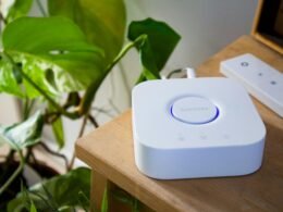 Ein Smart Home Hub und eine dazugehörige Fernbedienung liegen auf einem hellen Holztisch, technische Geräte für modernes Wohnen.