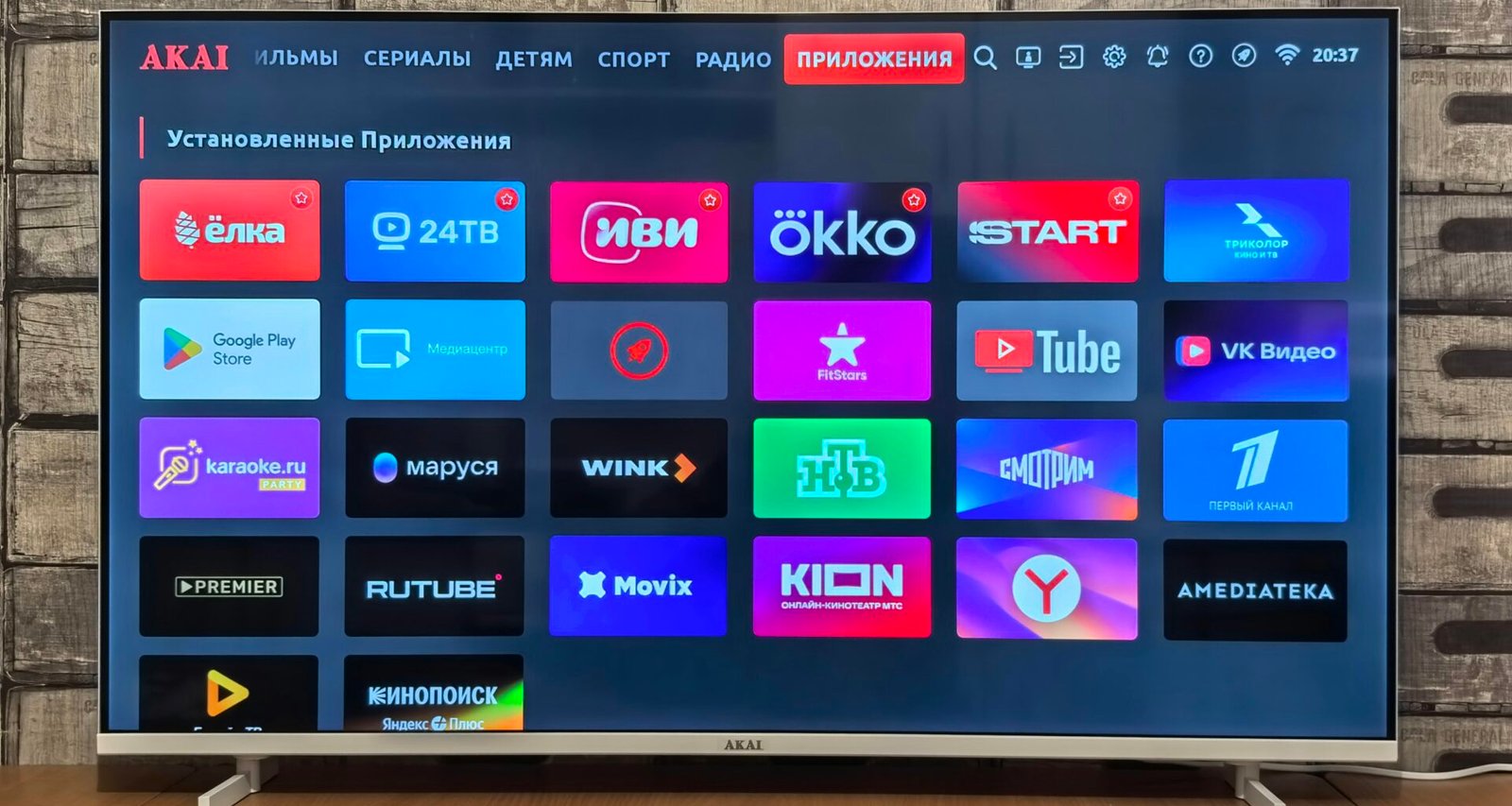 Smart TV Bildschirm mit verschiedenen App-Symbolen für Streaming, Spiele und Unterhaltung, fotografiert in moderner Wohnumgebung.