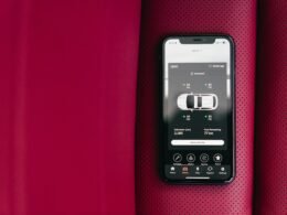 Ein Smartphone liegt auf einem roten Autositz und zeigt eine Car Control App zur Steuerung von Fahrzeugfunktionen.