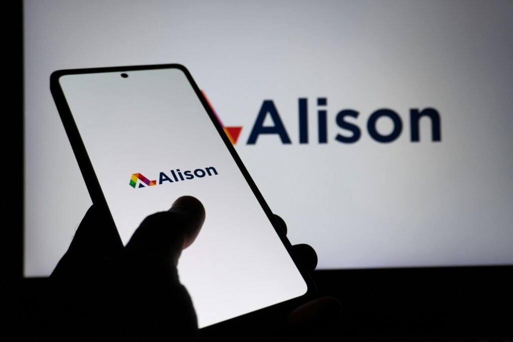 Hand hält Smartphone mit deutlich sichtbarem Alison Logo auf dem Bildschirm, Fokus auf mobile Lernplattformen