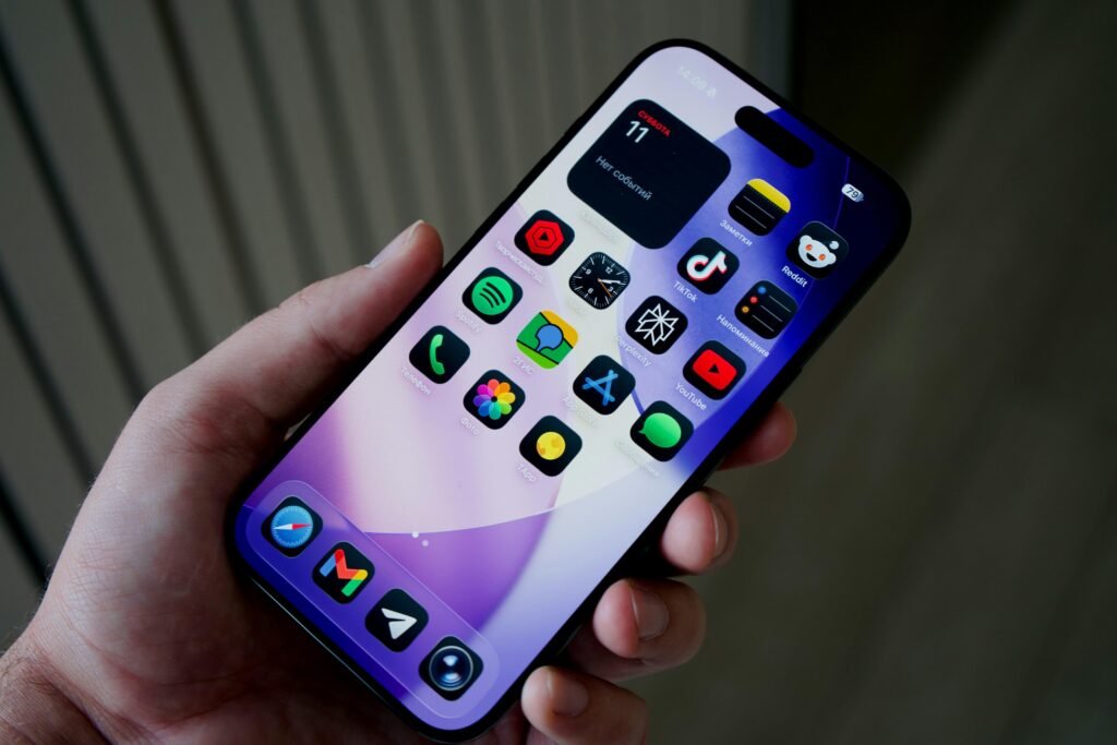 Hand hält Smartphone mit diversen farbigen App-Symbolen auf dem Display, dargestellt vor neutralem Hintergrund