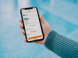 Person hält ein Smartphone in der Hand, auf dem eine Reise-App geöffnet ist, Fokus auf die mobile Anwendung.