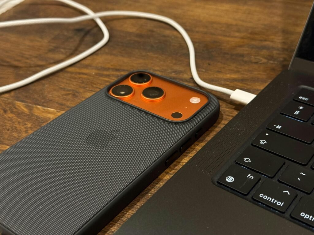 Ein Smartphone wird über ein Kabel mit einem Laptop verbunden. Beide Geräte liegen auf einem Tisch und sind eingeschaltet.