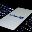 Smartphone mit LinkedIn-Logo liegt auf einer farbig beleuchteten Tastatur, Fokus auf modernes Networking im digitalen Umfeld