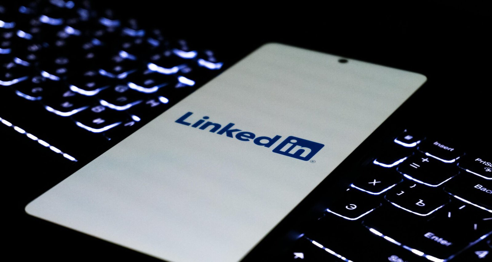 Smartphone mit LinkedIn-Logo liegt auf einer farbig beleuchteten Tastatur, Fokus auf modernes Networking im digitalen Umfeld