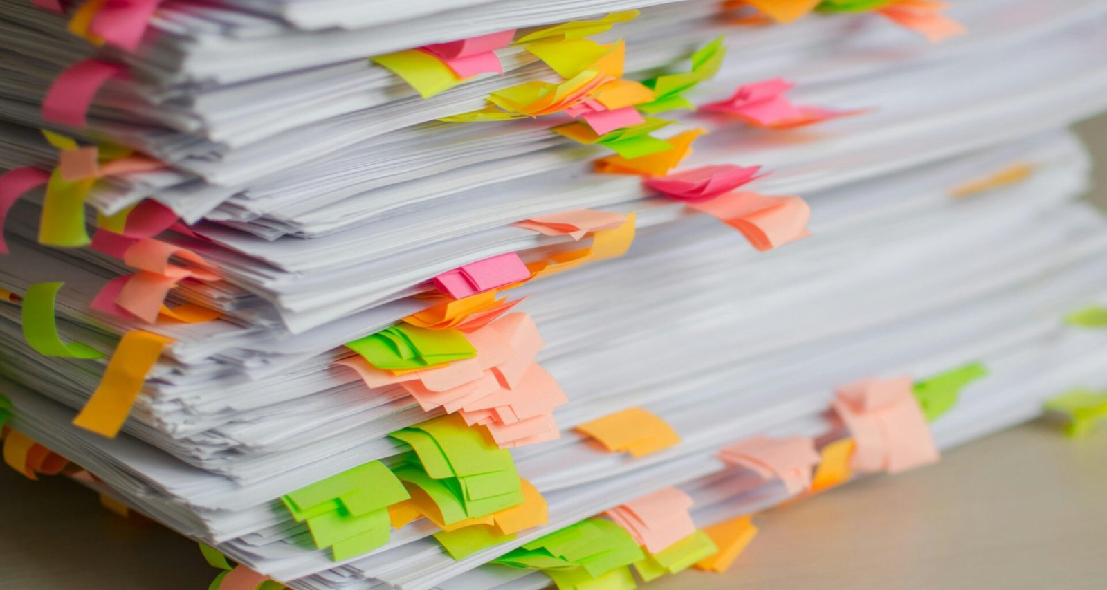 Ein Stapel Papier mit verschiedenfarbigen Klebezetteln zur Organisation von Unterlagen auf einem Schreibtisch