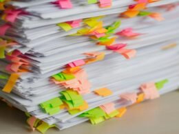 Ein Stapel Papier mit verschiedenfarbigen Klebezetteln zur Organisation von Unterlagen auf einem Schreibtisch