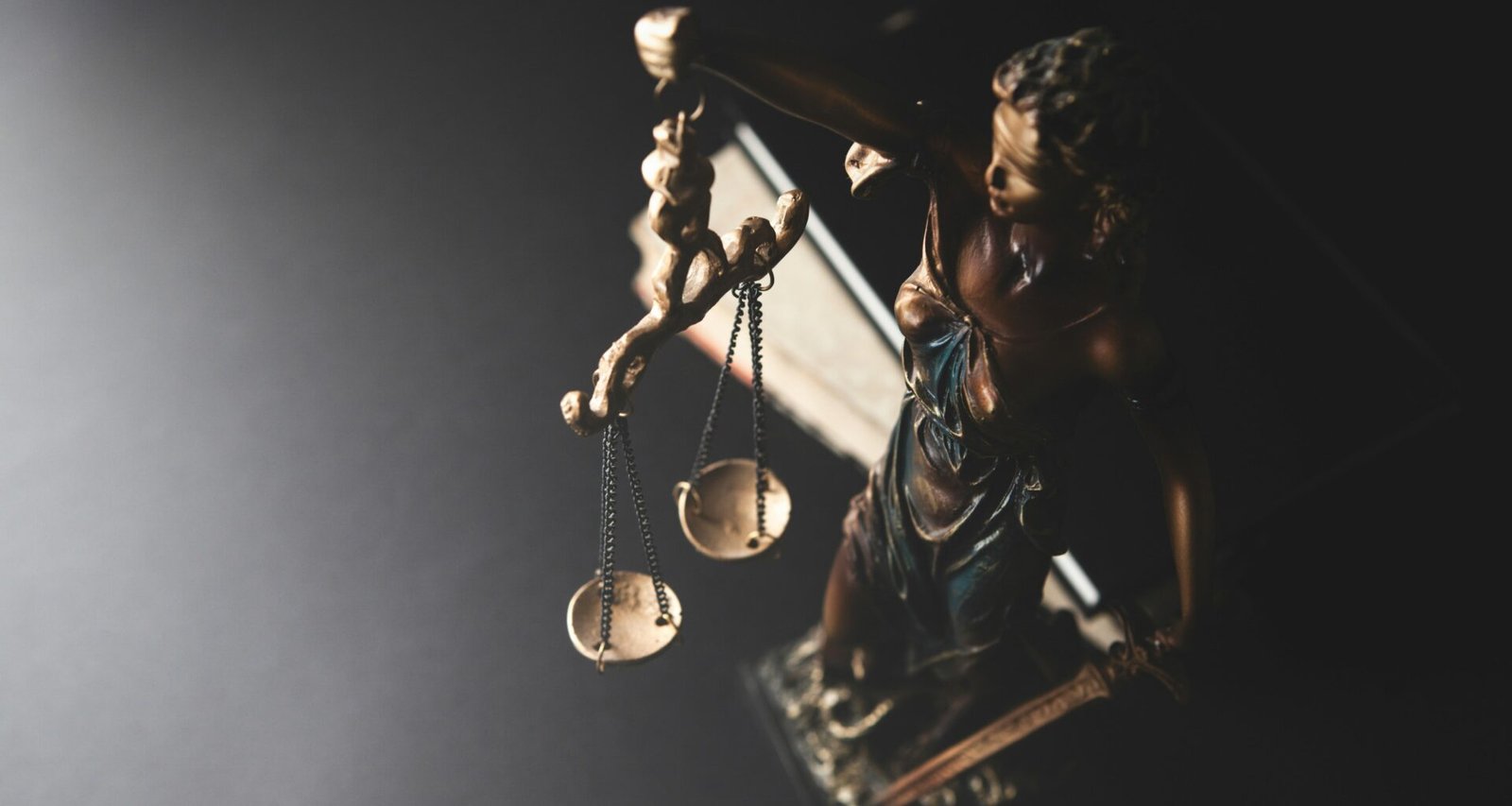 Statue der Justitia mit Waage auf dunklem Hintergrund, symbolisiert Recht und Gleichgewicht in einer juristischen Thematik.