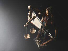 Statue der Justitia mit Waage auf dunklem Hintergrund, symbolisiert Recht und Gleichgewicht in einer juristischen Thematik.