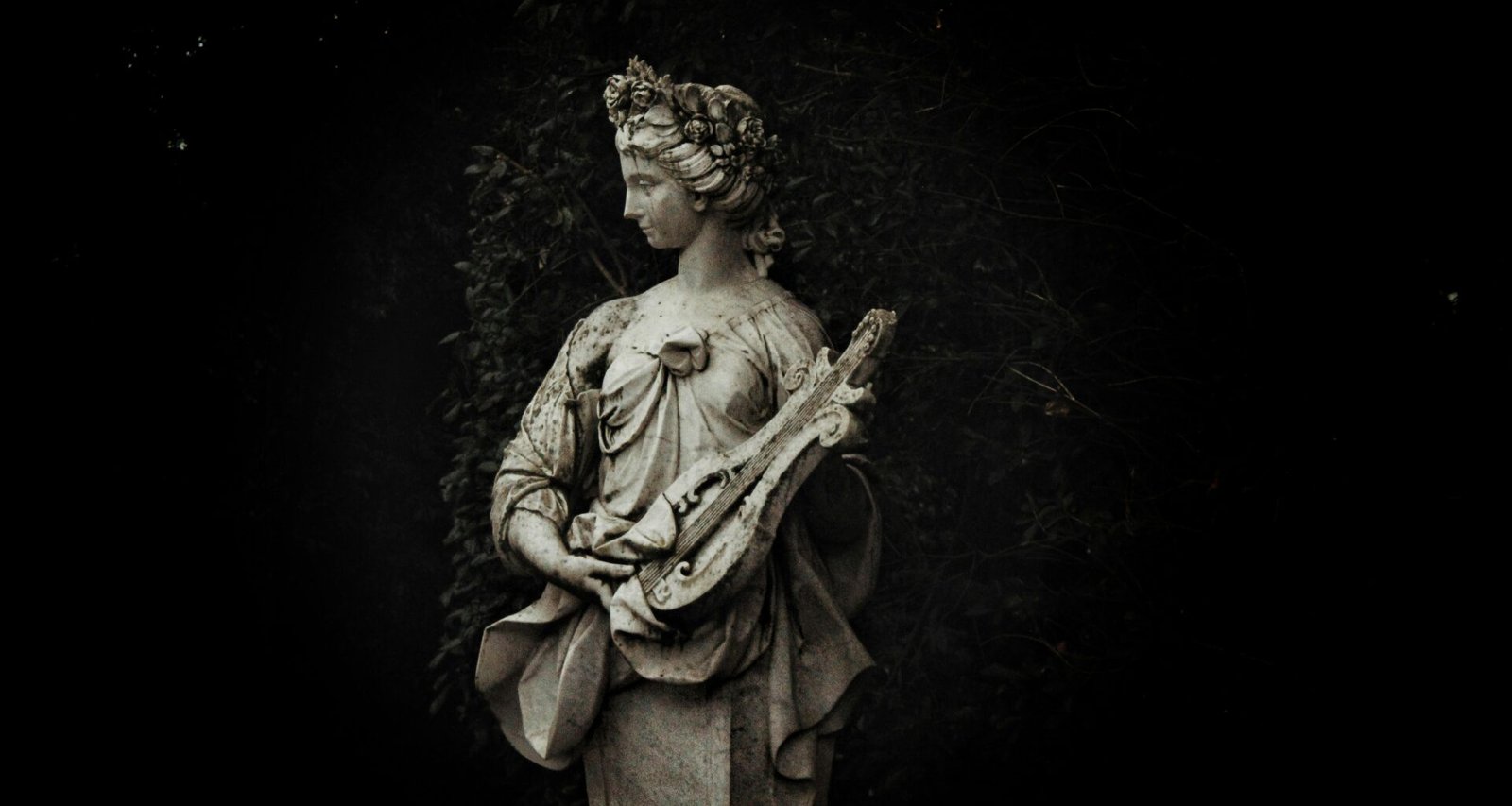 Statue einer Frau hält eine Laute und steht umgeben von Gartenpflanzen im Freien