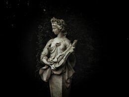 Statue einer Frau hält eine Laute und steht umgeben von Gartenpflanzen im Freien