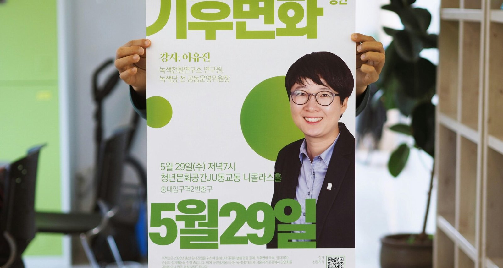 Stehende Person hält ein Poster mit dem Bild eines lächelnden Mannes sowie Texten in koreanischer Schrift