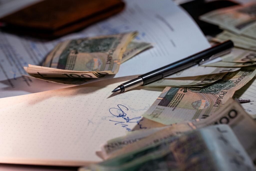 Mehrere Geldscheine und ein Kugelschreiber liegen verstreut auf ausgedruckten Finanzdokumenten sowie Berichten.