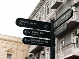 Mehrere Straßenschilder, die an einem Gebäude angebracht sind und in unterschiedliche Richtungen zeigen