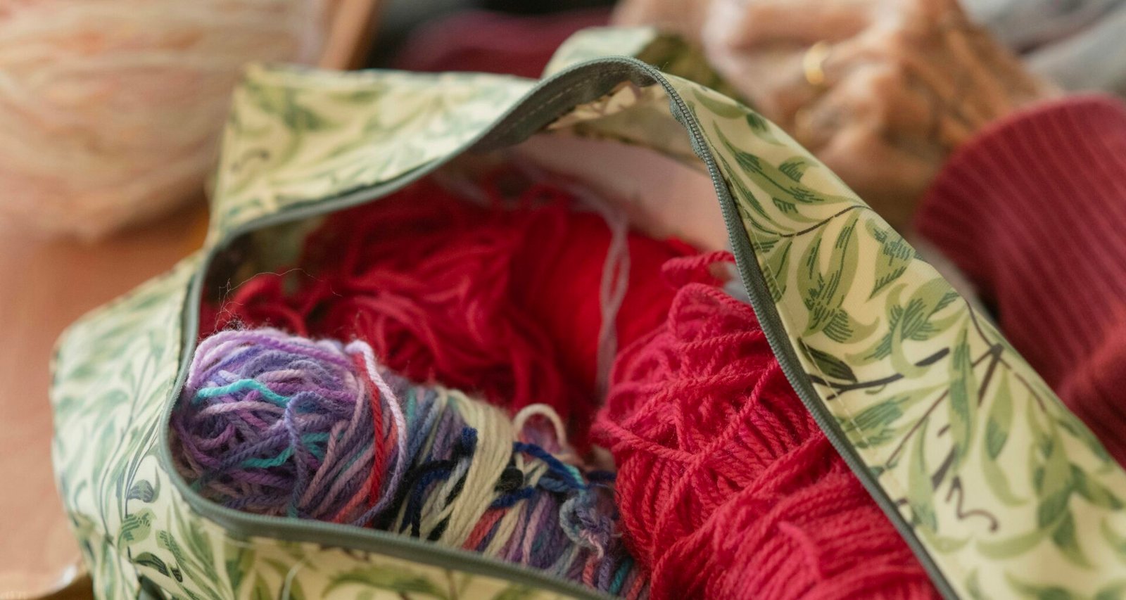 Eine geöffnete Tasche, gefüllt mit bunten Wollknäueln, Stricknadeln und weiterem Strickzubehör auf einer Oberfläche