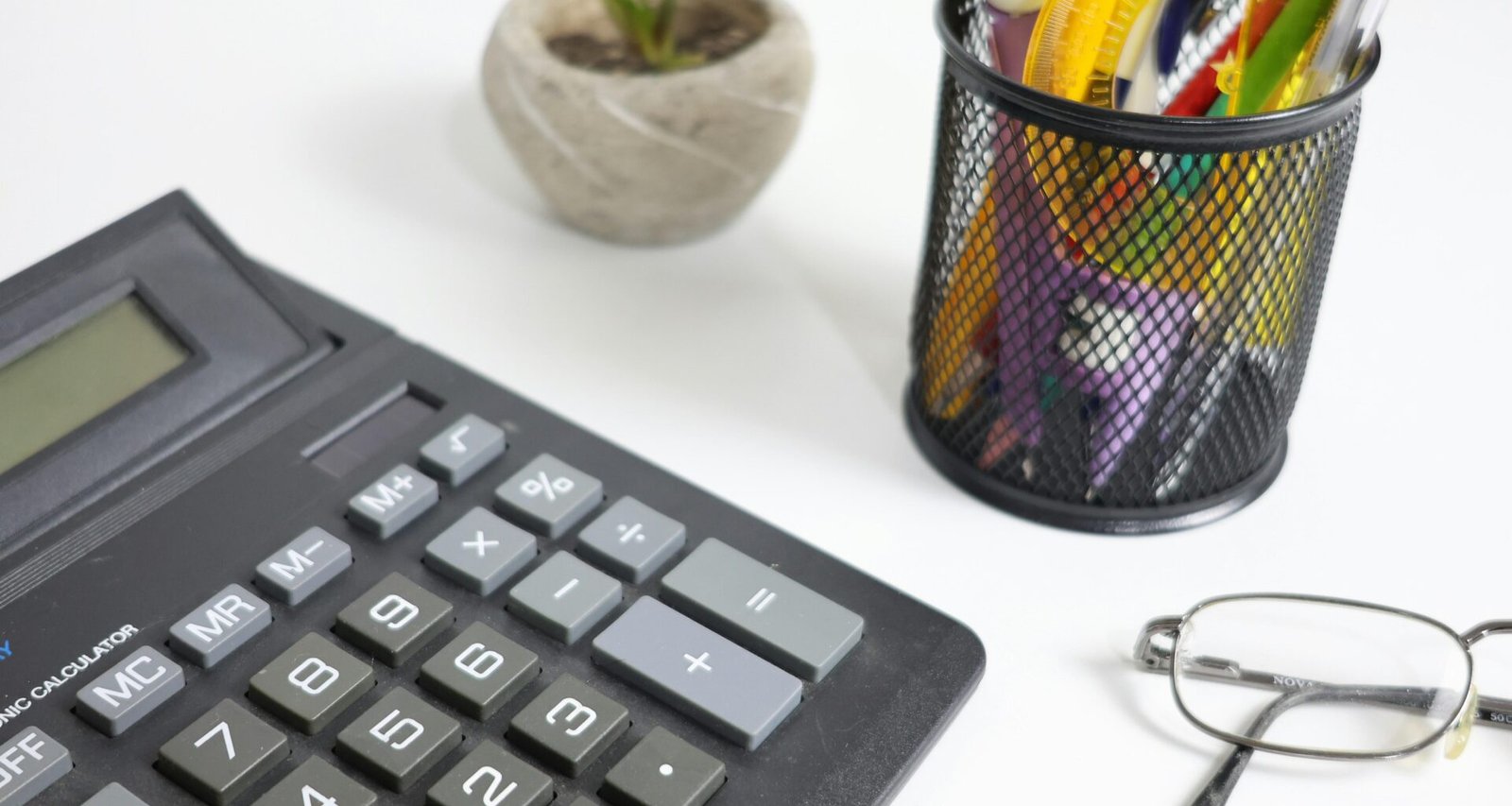 Taschenrechner, Brille und Stifte liegen ordentlich auf einem weißen Schreibtisch für effizientes Arbeiten und Organisation.