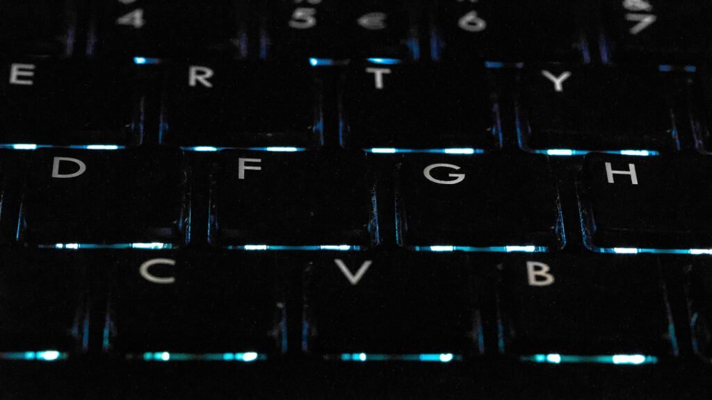 Detailaufnahme einer schwarzen hintergrundbeleuchteten Tastatur auf einem Schreibtisch als Symbol für moderne Technik