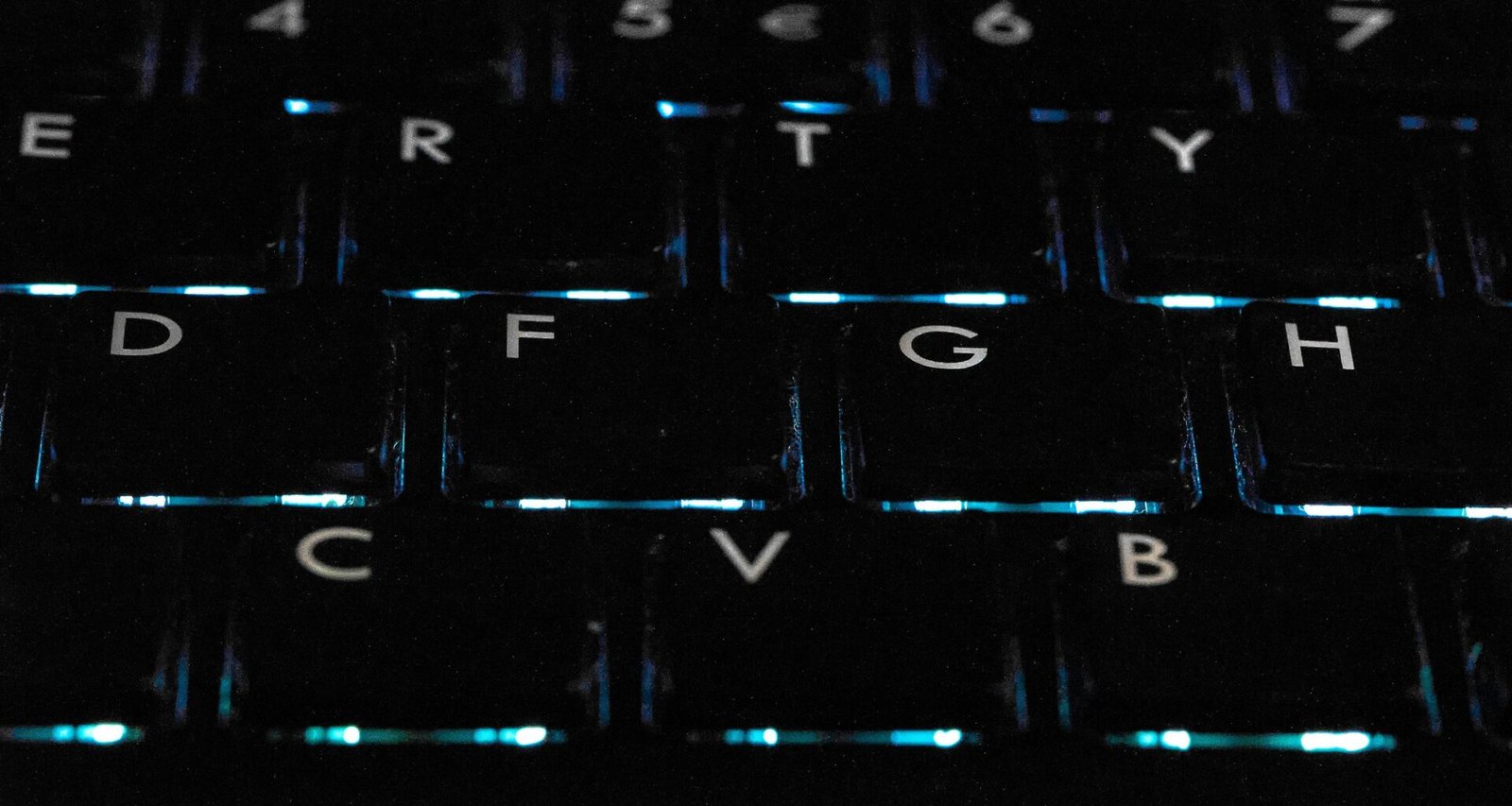 Detailaufnahme einer schwarzen hintergrundbeleuchteten Tastatur auf einem Schreibtisch als Symbol für moderne Technik
