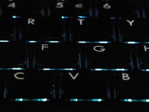Detailaufnahme einer schwarzen hintergrundbeleuchteten Tastatur auf einem Schreibtisch als Symbol für moderne Technik