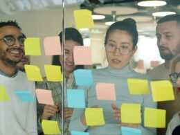 Ein Team diskutiert und plant an einer Glaswand mit zahlreichen farbigen Haftnotizen während einer Brainstorming-Session.