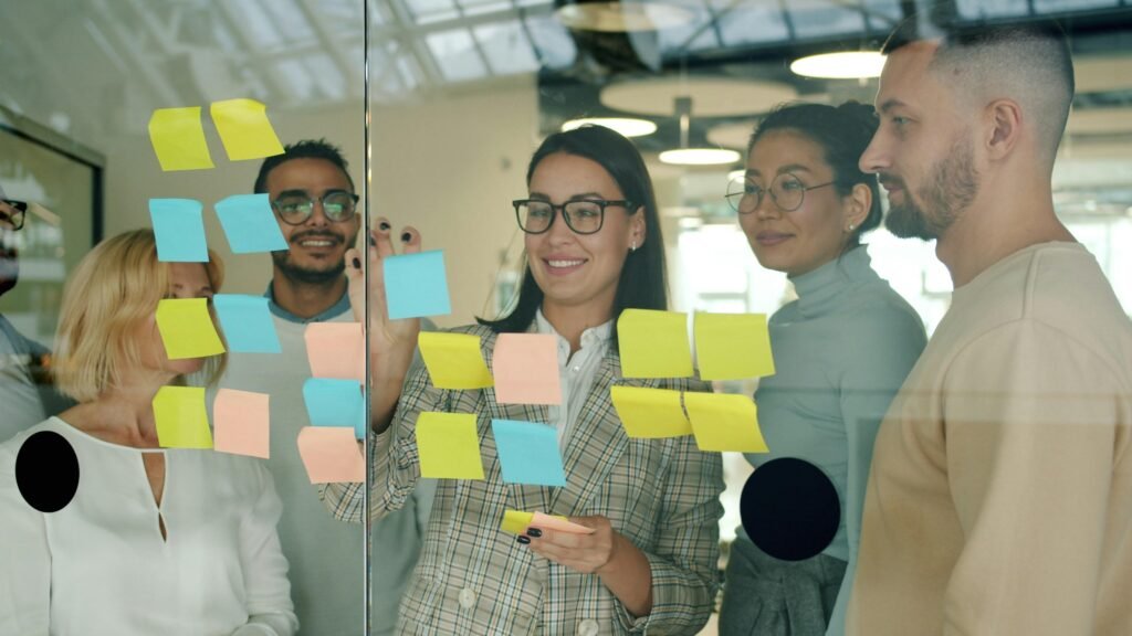 Mehrere Teammitglieder besprechen Konzepte und Ideen mit Haftnotizen auf einer Glaswand im modernen Büro.