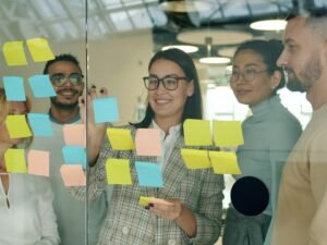 Mehrere Teammitglieder besprechen Konzepte und Ideen mit Haftnotizen auf einer Glaswand im modernen Büro.