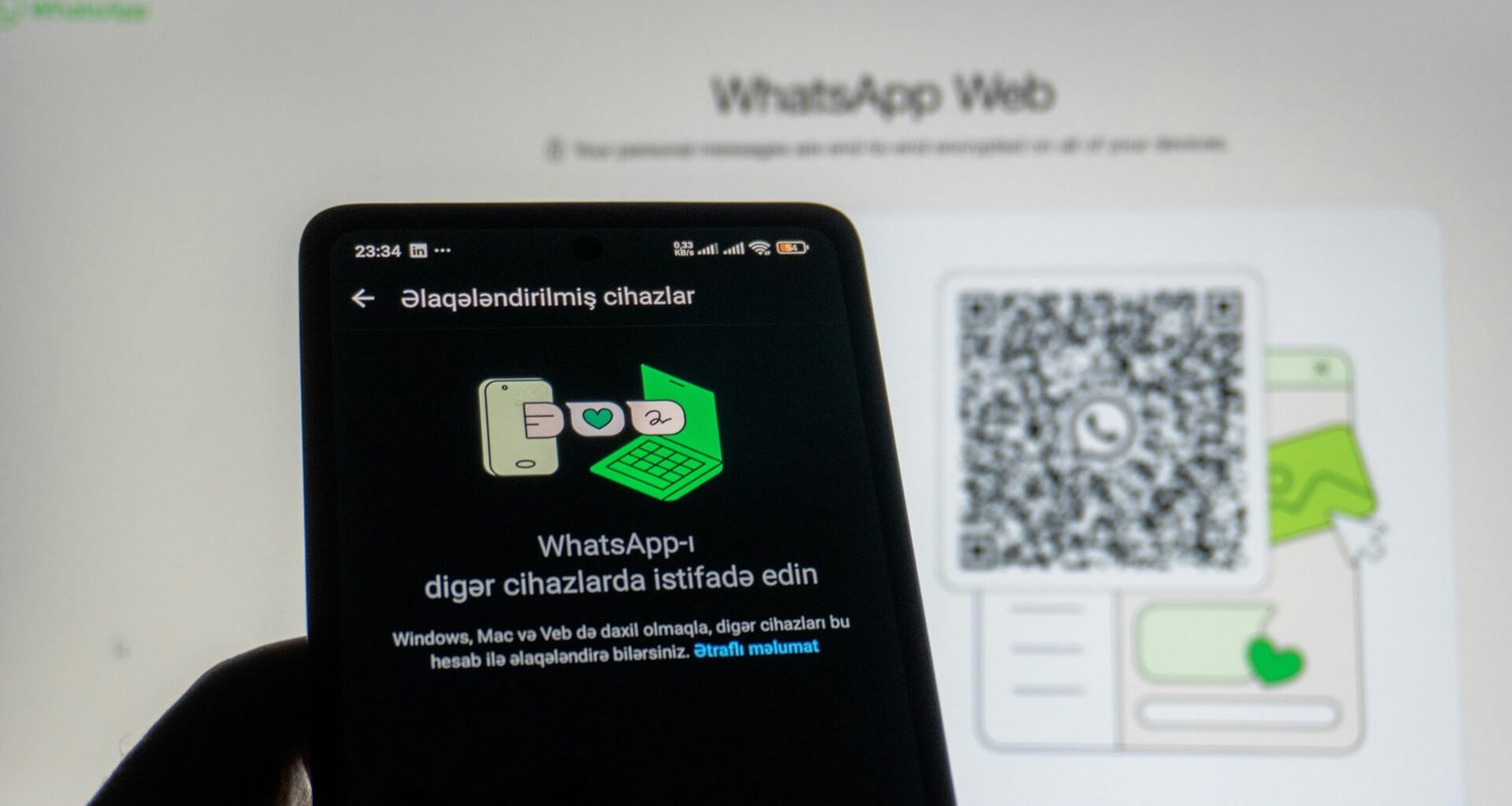 Hand hält ein Smartphone vor einen Computerbildschirm und scannt den WhatsApp Web QR-Code, um die Verbindung herzustellen
