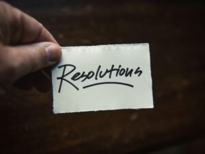 Laptop und Smartphone liegen auf einem hellen Holztisch, Bürobedarf im Hintergrund, Fokus auf technische Geräte