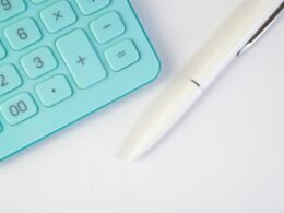 Türkiser Taschenrechner und weißer Stift liegen auf weißem Hintergrund für Themen wie Online-Marketing und digitales Arbeiten