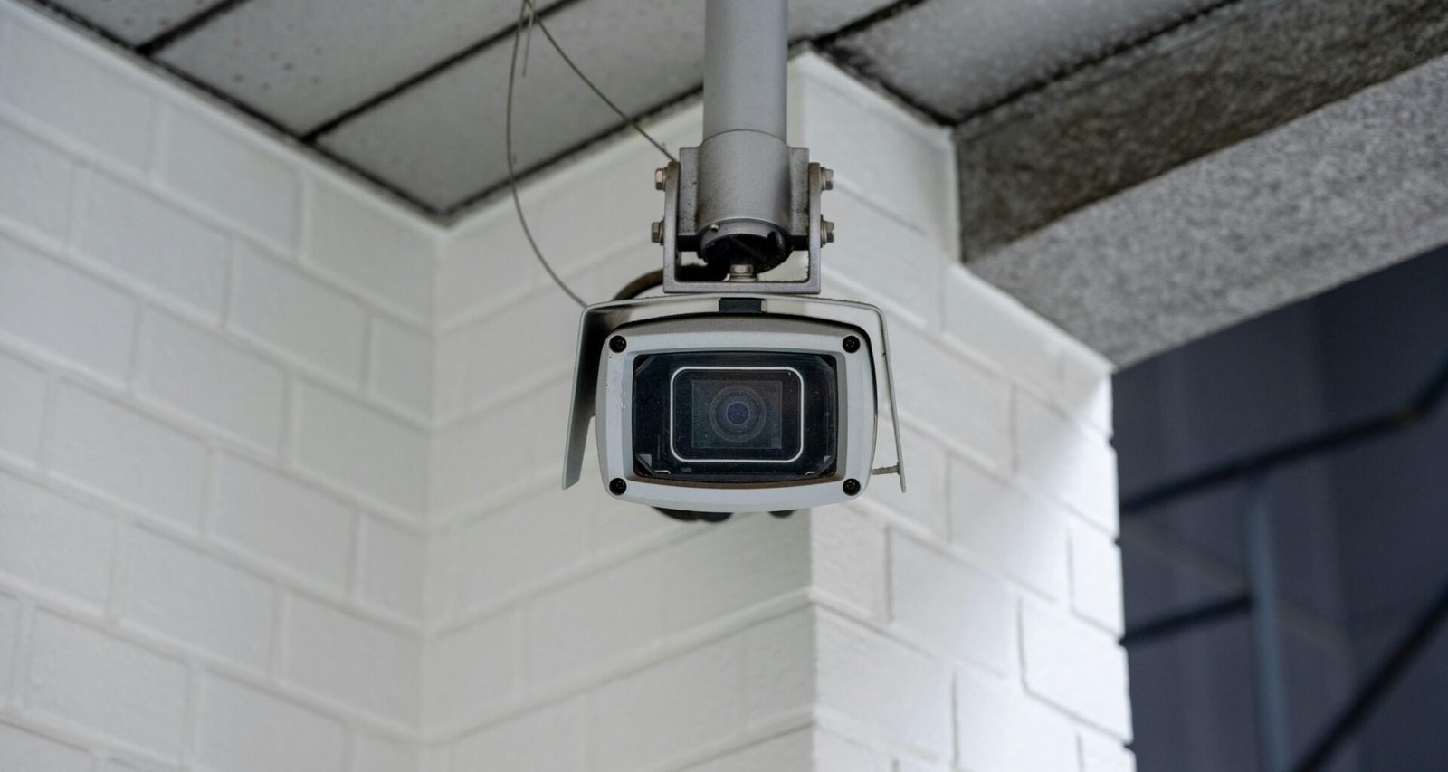 Sicherheitskamera ist an einer weißen Backsteinwand montiert und überwacht den Bereich vor der Wand.