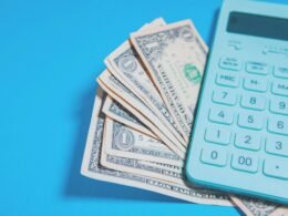 US-Dollar-Scheine und ein schwarzer Taschenrechner nebeneinander auf einem blauen Hintergrund angeordnet