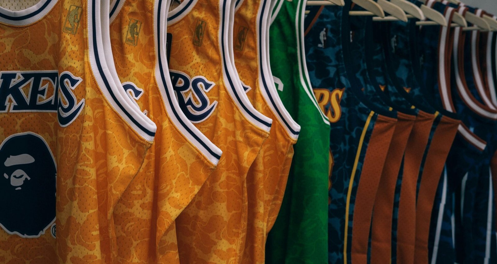Mehrere NBA-Trikots unterschiedlicher Teams hängen ordentlich auf Kleiderbügeln in einer Reihe an einer Kleiderstange.