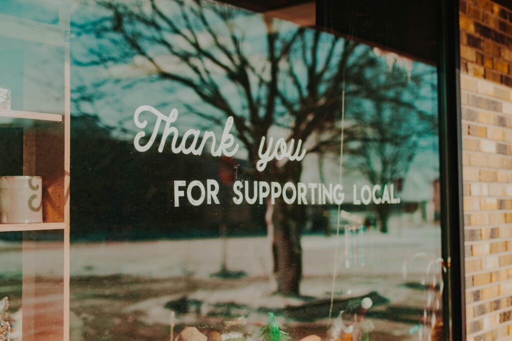 Schild „Thank you for supporting local“ an einem Schaufenster mit Reflexionen im Glas, Unterstützung lokaler Unternehmen