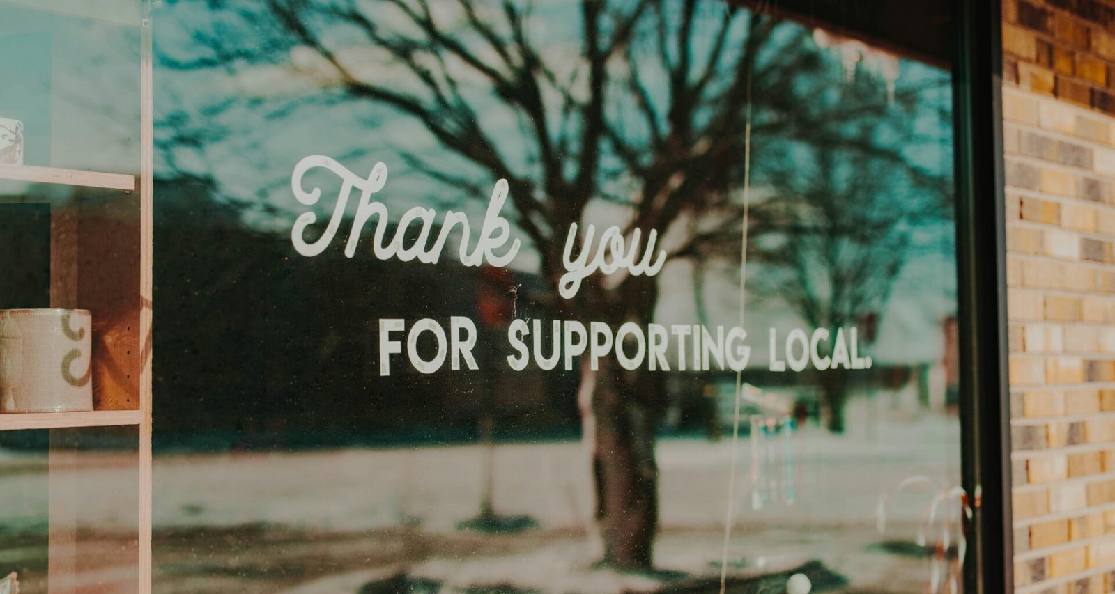 Schild „Thank you for supporting local“ an einem Schaufenster mit Reflexionen im Glas, Unterstützung lokaler Unternehmen