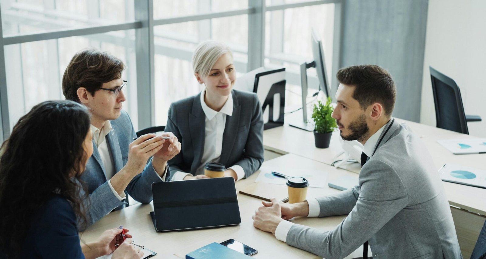 Mehrköpfiges diverses Business-Team arbeitet zusammen an einem großen Tisch in einem modernen Büro mit Laptops und Unterlagen.