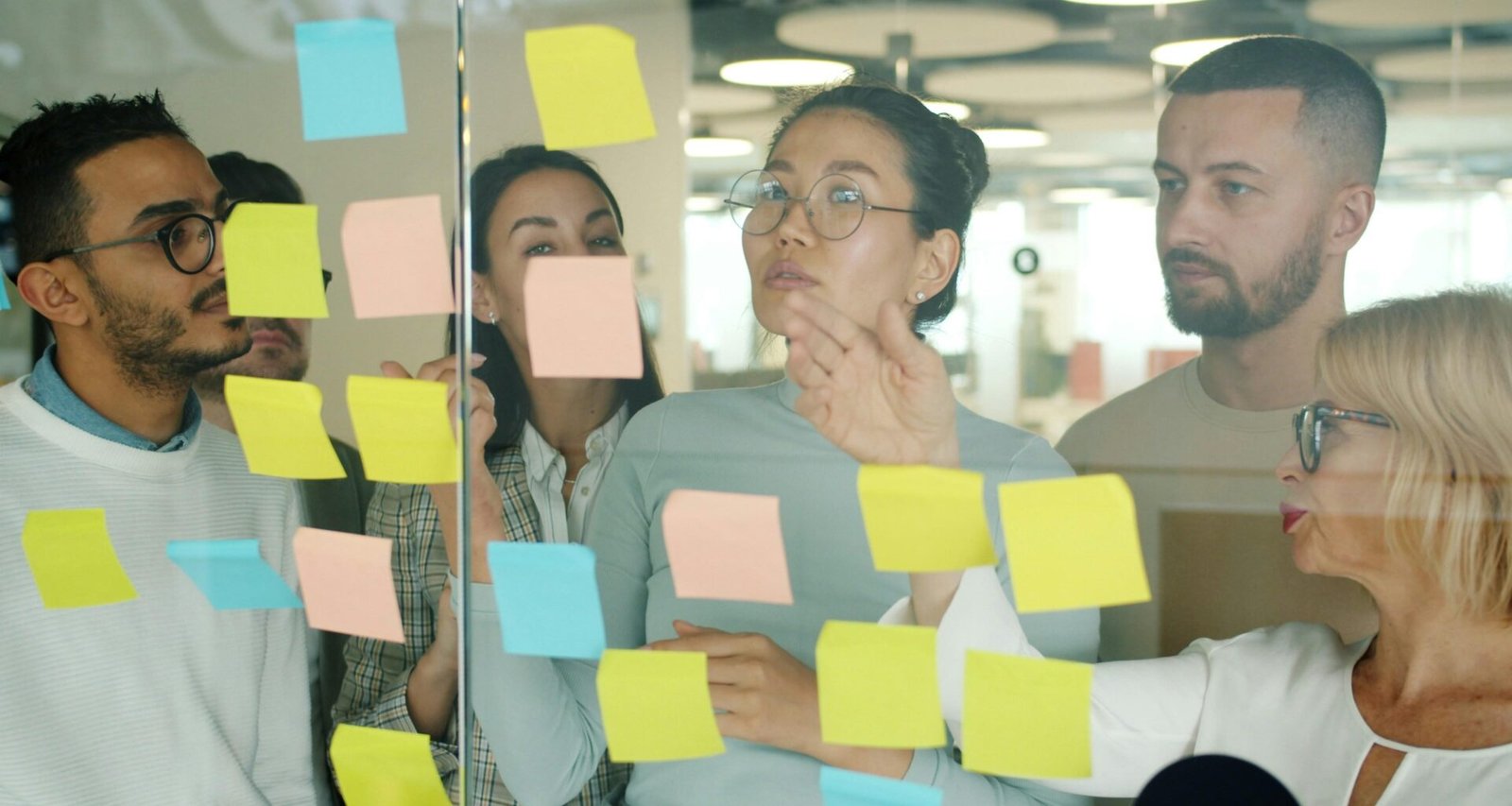 Ein diverses Team arbeitet zusammen und ordnet bunte Klebezettel auf einem Tisch, um Ideen zu strukturieren.