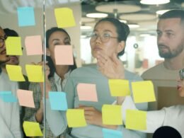 Ein diverses Team arbeitet zusammen und ordnet bunte Klebezettel auf einem Tisch, um Ideen zu strukturieren.